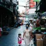 a woman and her daughter walk down a street in bangkok, thailand.