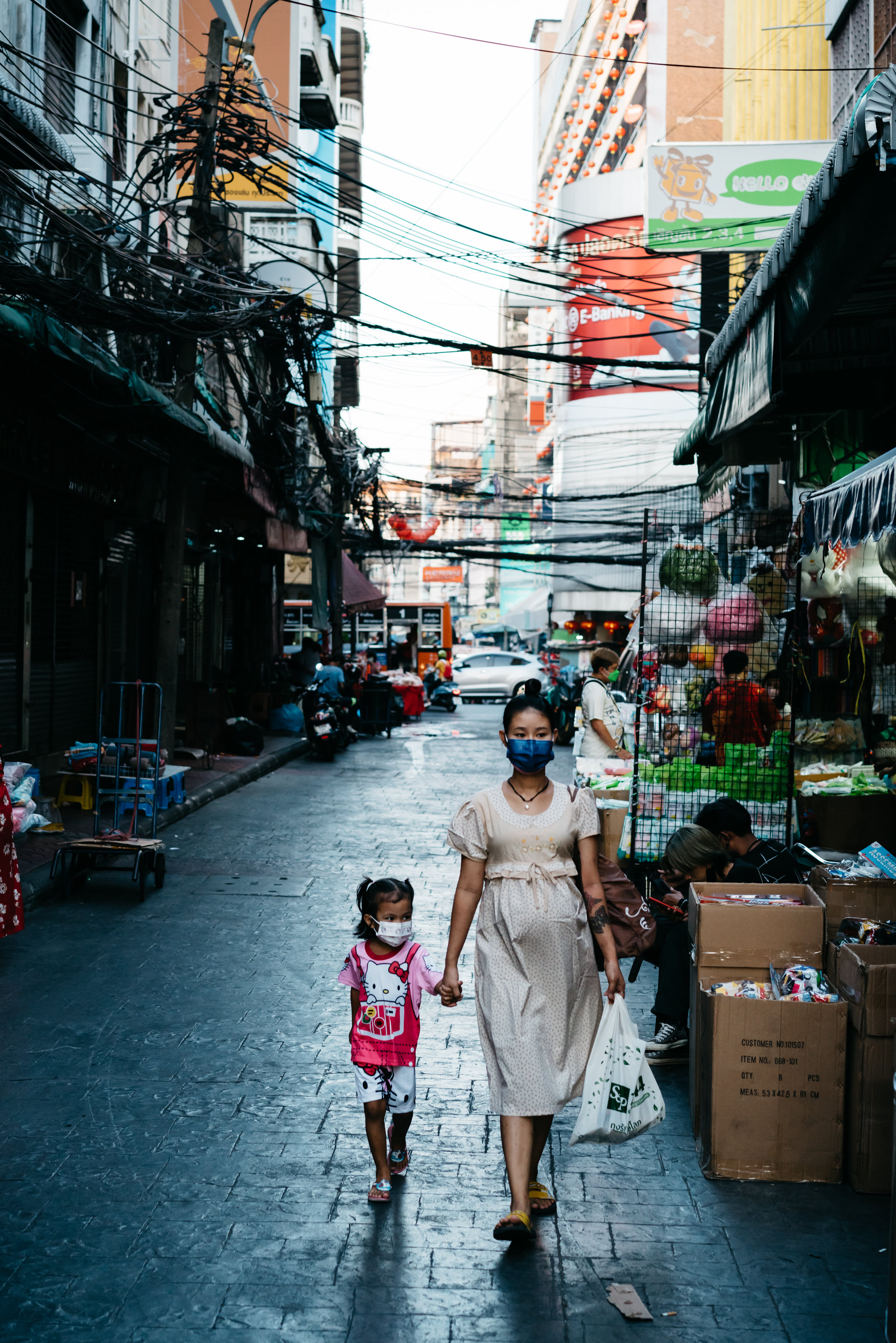 a woman and her daughter walk down a street in bangkok, thailand.