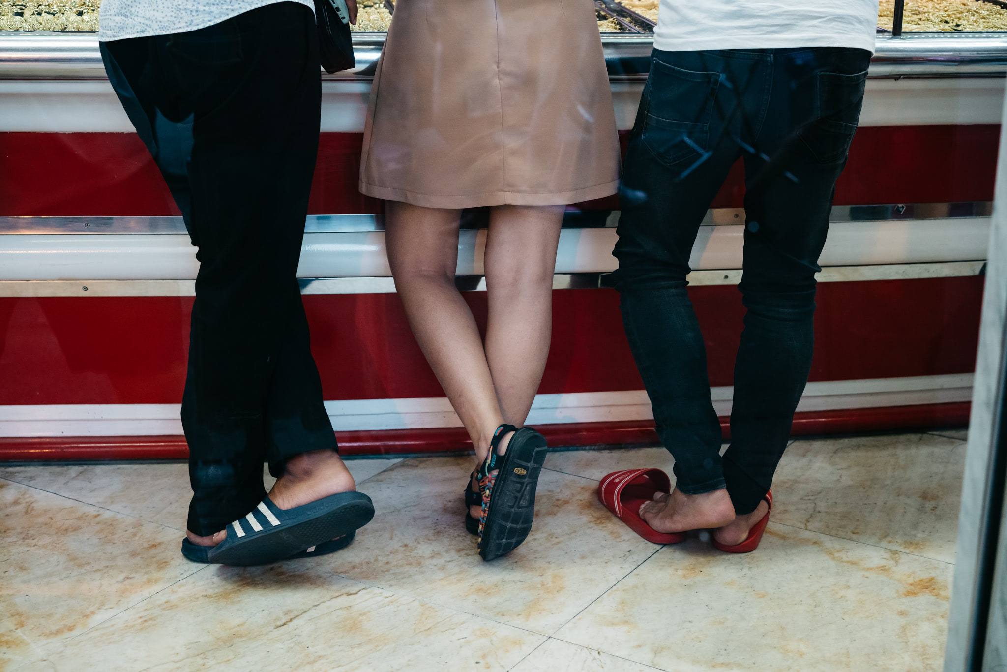 three people standing in front of a counter top with a woman in a tan skirt