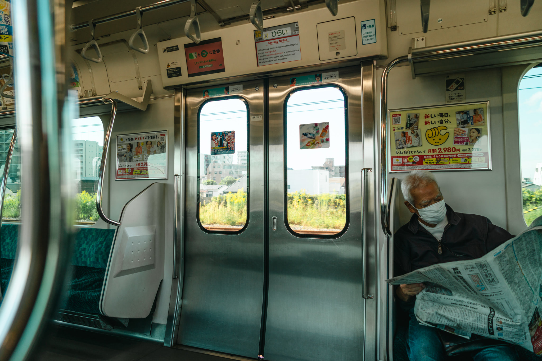 Inside view of a Japanese train with a person reading a newspaper