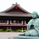 Traditional Japanese temple with red accents and a statue in front