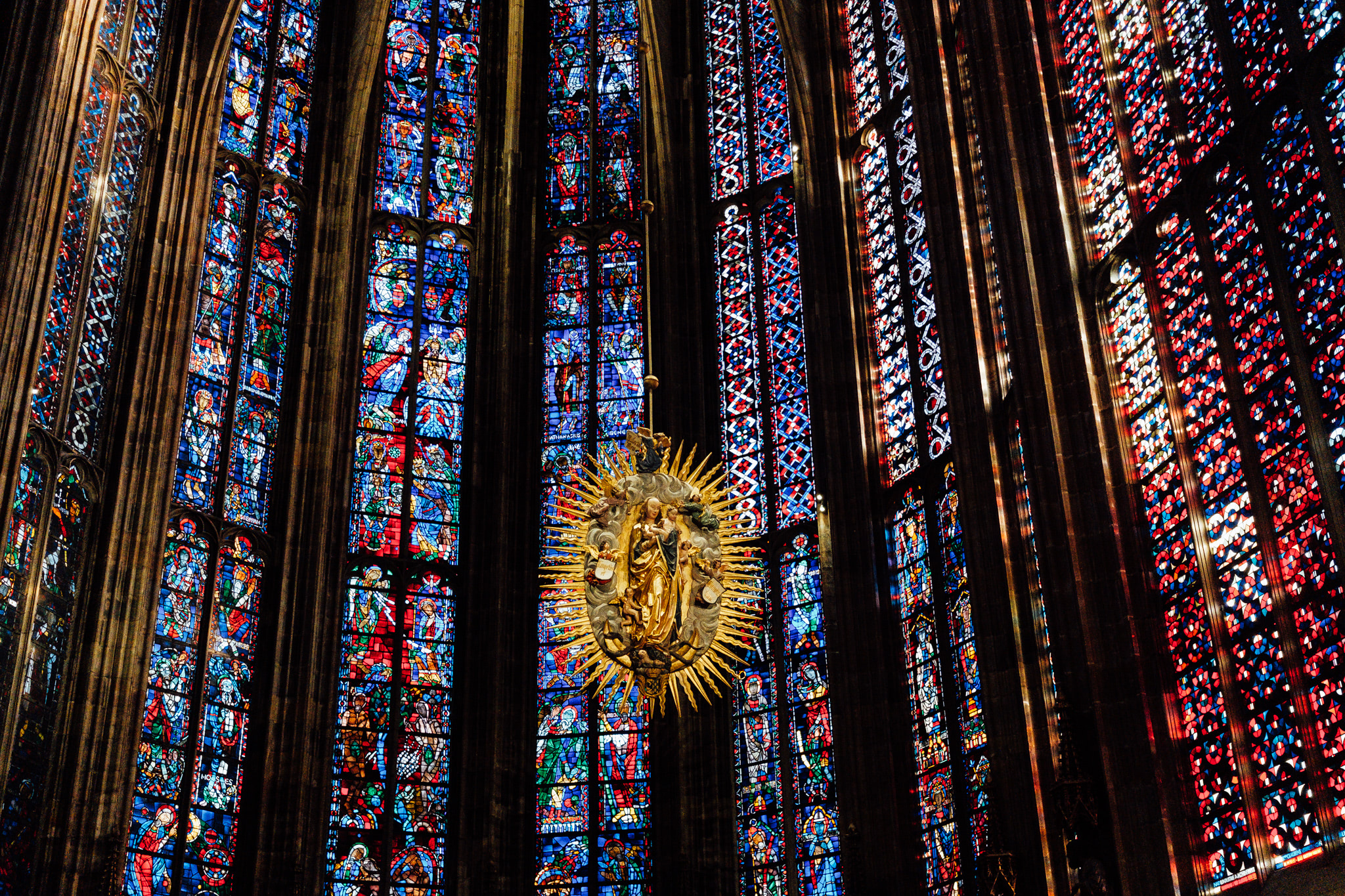 Aachen Cathedral's interior with colorful stained-glass windows and a golden Madonna and Child sculpture.