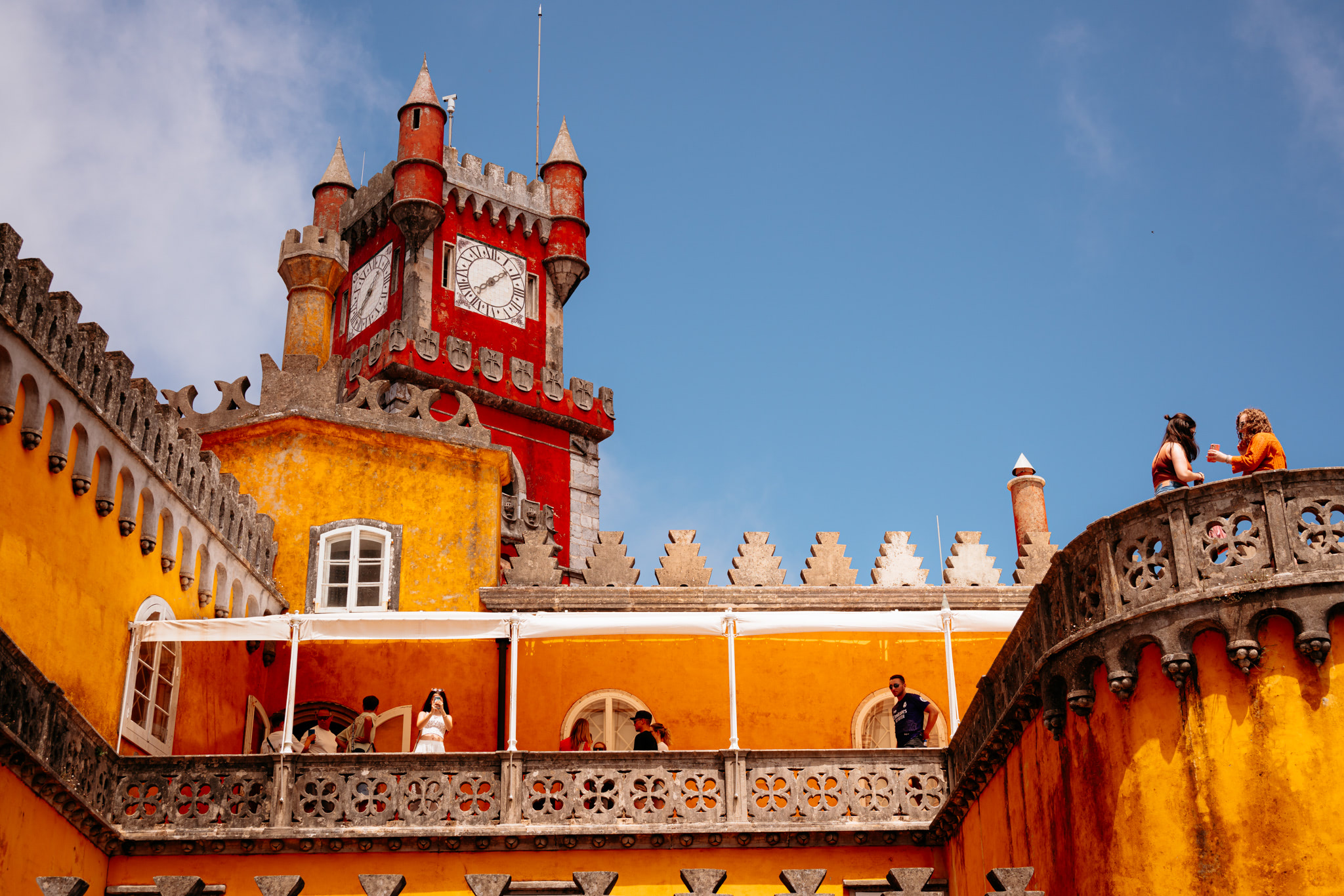 Pena Palace in Portugal, featuring a vibrant yellow and red exterior, clock tower, and people on a balcony.