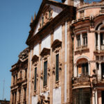 Two adjacent historic buildings in Porto, Portugal, one stone and one peach-colored, both ornate.